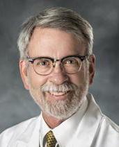 man wearing glasses and a white lab coat, smiling at the camera