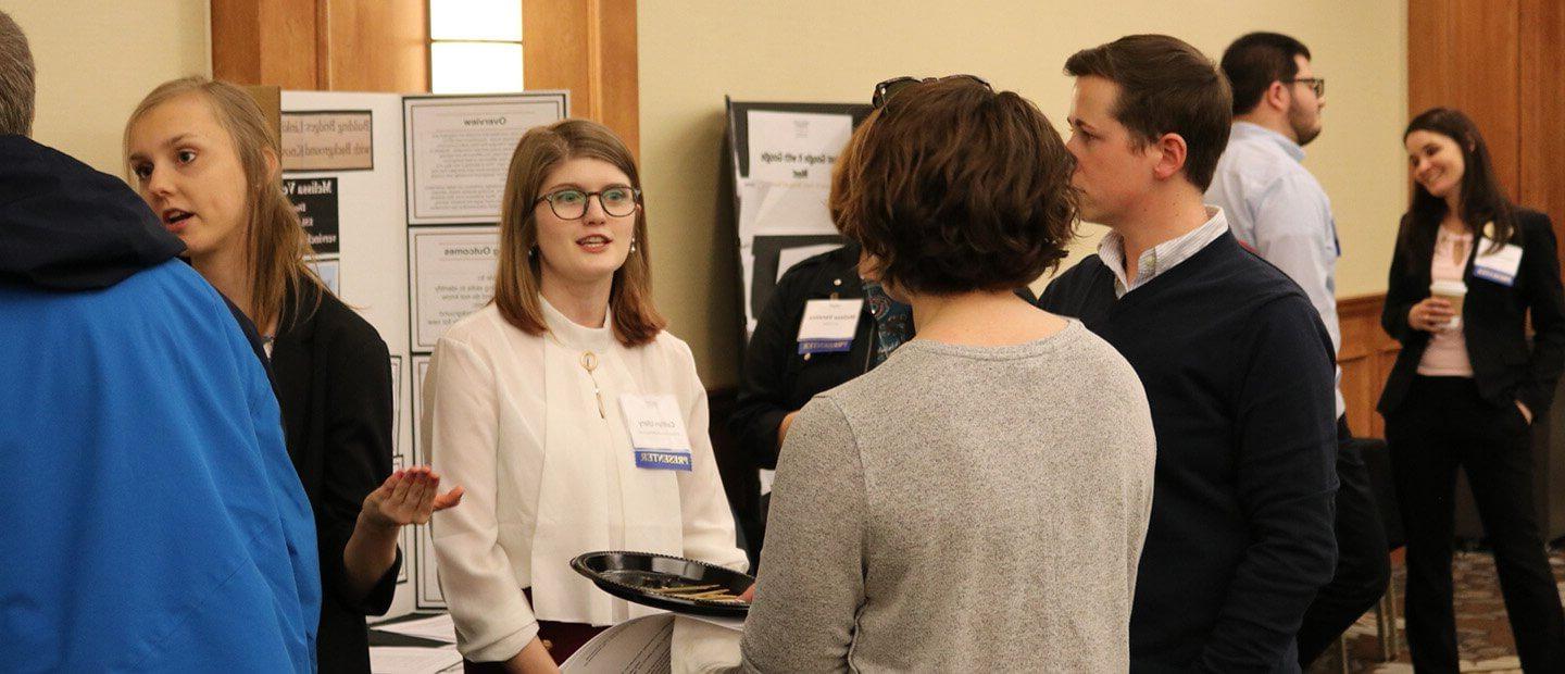 Adults in professional clothing viewing and discussing poster presentations in a conference room.